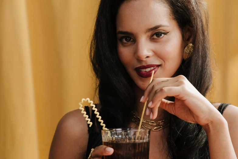 a close up of a person holding a drink, inspired by Ceferí Olivé, trending on pexels, renaissance, indian girl with brown skin, black jewellery, straw, vintage inspired