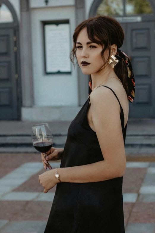 a woman in a black dress holding a glass of wine, by Niko Henrichon, pexels contest winner, long earrings, on the sidewalk, wearing black camisole outfit, black marble and gold