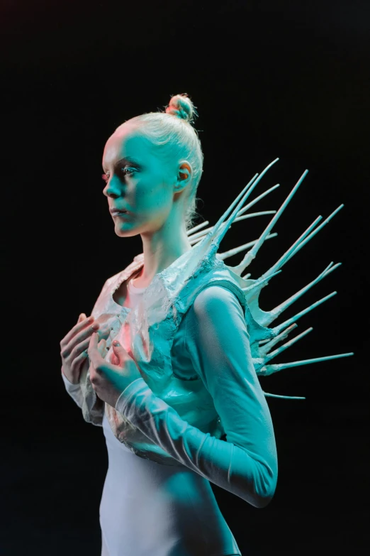 a woman standing in front of a black background, a surrealist sculpture, inspired by Ignacy Witkiewicz, elle fanning as an android, ribcage, white and teal garment, concert