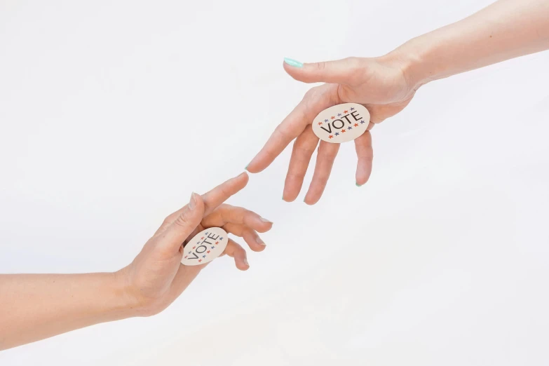 two hands reaching for a button with the word vote on it, by Arabella Rankin, trending on pexels, interactive art, photoshoot for skincare brand, bone jewellery, set against a white background, woman holding another woman