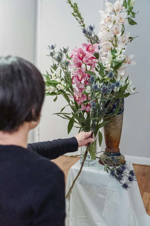 a woman placing flowers in a vase on a table, soft blue and pink tints, overgrown with orchids, ready to model, large tall
