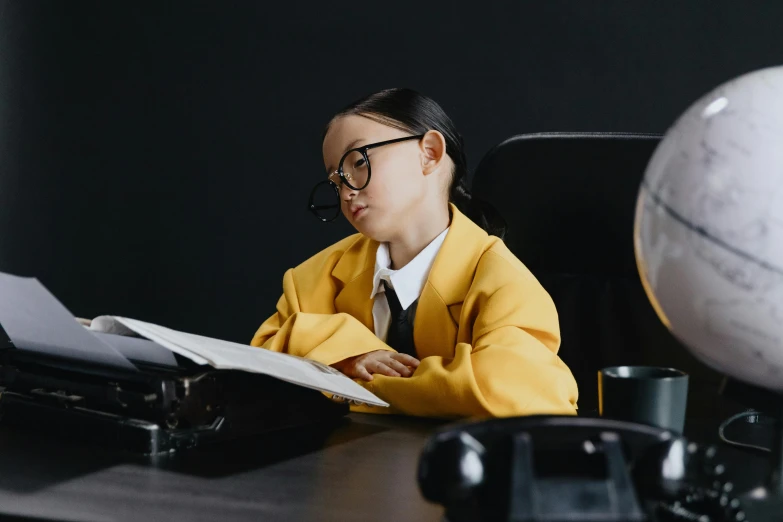 a little girl sitting at a desk in front of a globe, pexels contest winner, in suit with black glasses, lady using yellow dress, wearing a school uniform, avatar image