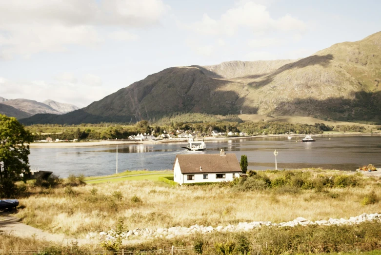 a house next to a body of water with mountains in the background, inspired by Arthur Melville, unsplash, hurufiyya, scottish style, 1970s photo, conde nast traveler photo, harbour