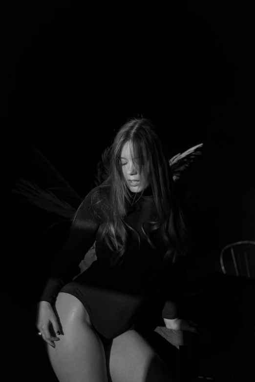 a woman sitting on a chair in the dark, a black and white photo, unsplash, conceptual art, hailee steinfeld, with wings, album cover, looks like young liv tyler
