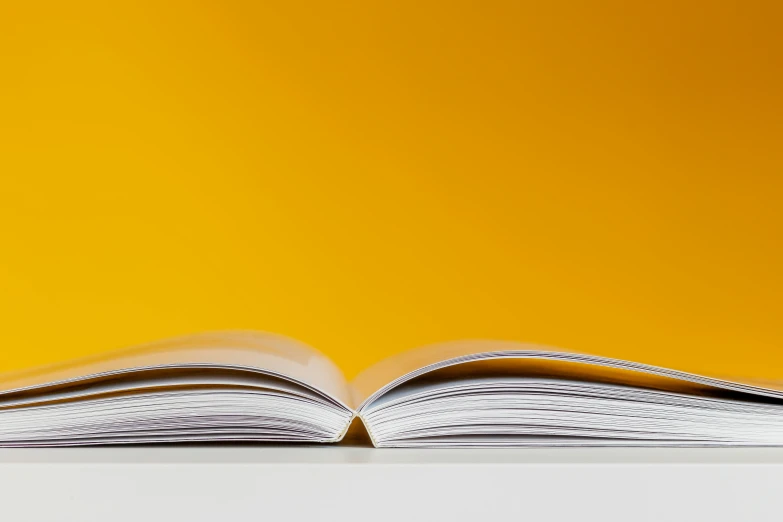 an open book sitting on top of a table, a picture, by Julian Allen, unsplash, yellow backdrop, 3/4 view from below, lpoty, white and yellow scheme