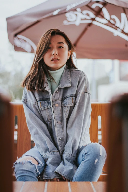 a woman sitting on top of a wooden bench, by Robbie Trevino, trending on pexels, photorealism, denim jacket, beautiful asian woman sitting, pastel clothing, streetwear