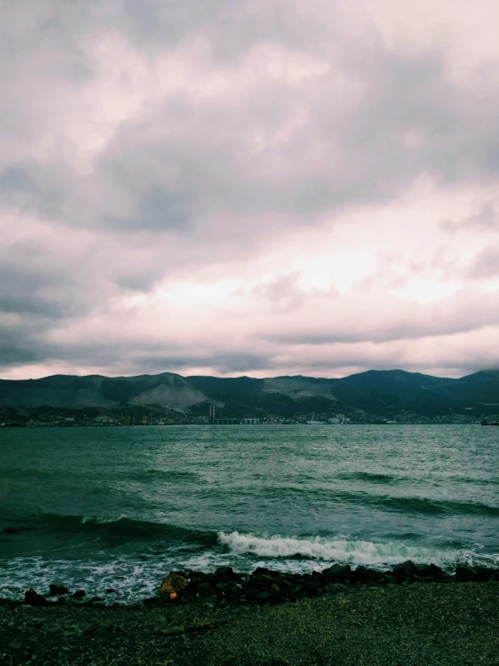 a person flying a kite on top of a beach, a picture, inspired by Elsa Bleda, unsplash, romanticism, big overcast, hills and ocean, the city of santa barbara, dark green water