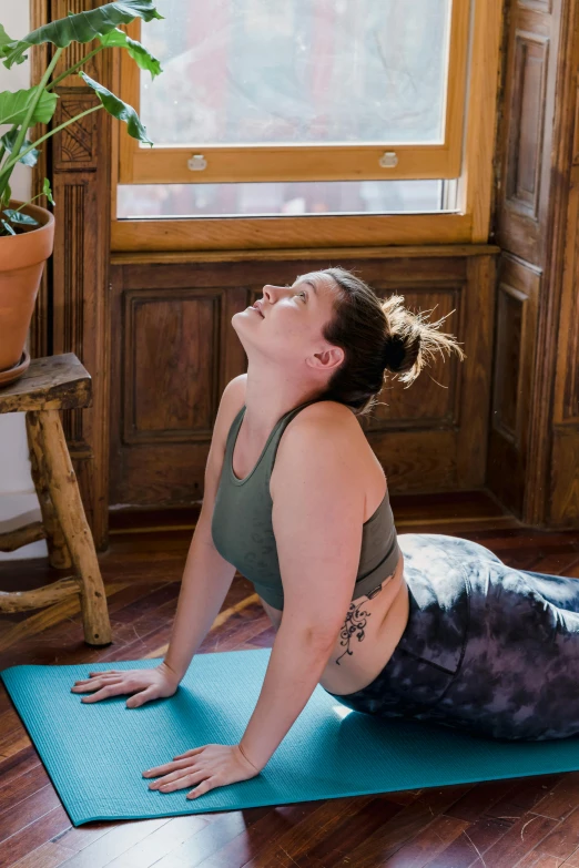 a woman doing a yoga pose on a yoga mat, a portrait, by Jessie Algie, pexels contest winner, renaissance, thicc, head tilted down, next to window, low quality photo