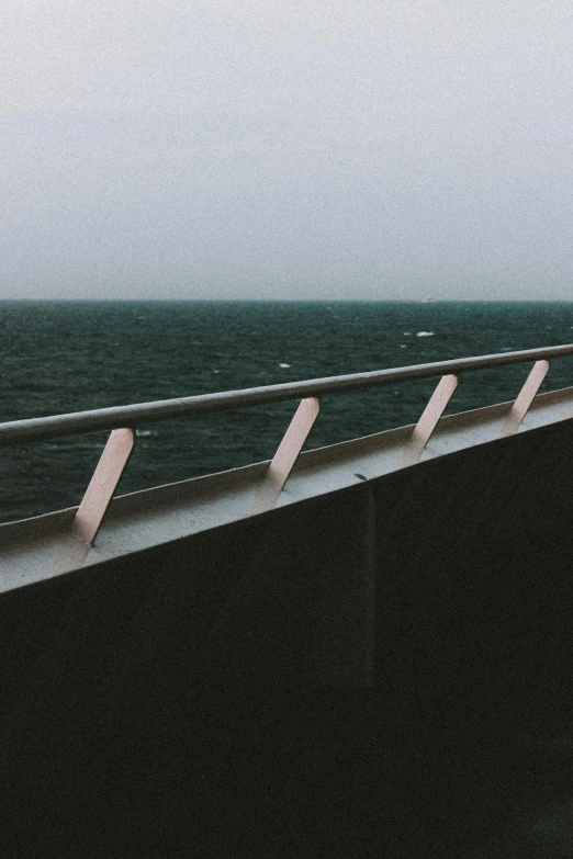 a man standing on top of a bridge next to the ocean, inspired by Elsa Bleda, unsplash, postminimalism, dreary, railing, on a boat, highway