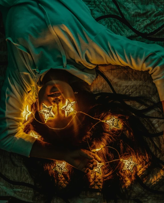 a woman laying in bed with christmas lights on her head, an album cover, inspired by Elsa Bleda, pexels contest winner, conceptual art, with glowing runes on the body, glowing yellow face, dark and grim lighting, top down view