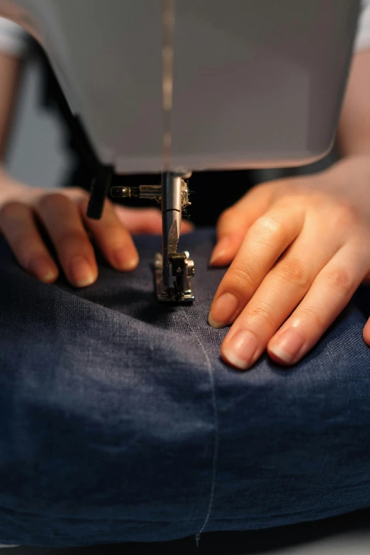 a close up of a person using a sewing machine, wearing a dark shirt and jeans, a blue skirt, artsation, raising an arm