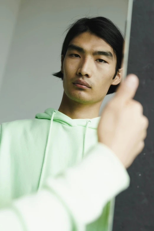 a man in a green hoodie pointing at a blackboard, inspired by Fei Danxu, trending on unsplash, at a fashion shoot, light green, asian face, thumb up