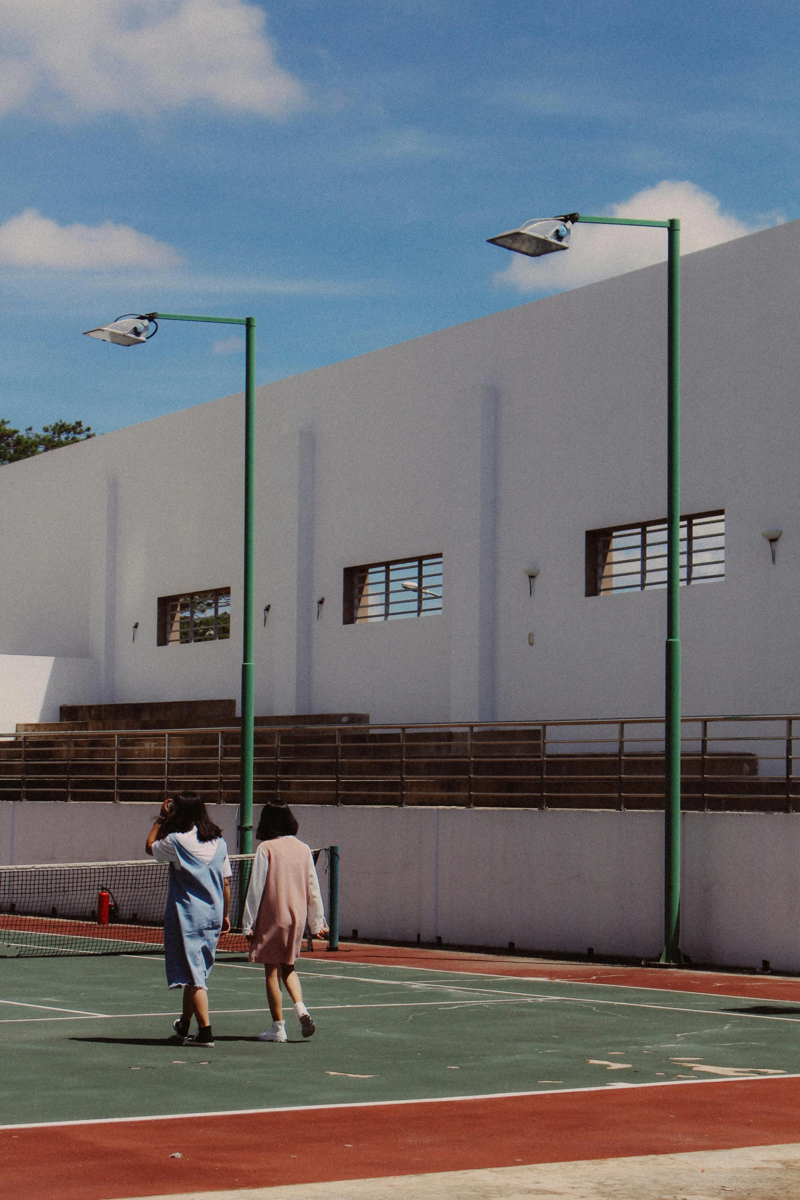 a couple of people standing on top of a tennis court, unsplash, conceptual art, street lamps, school courtyard, wide film still, promo image