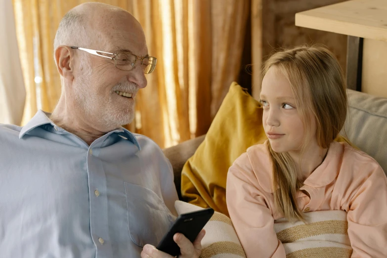 a man sitting next to a little girl on a couch, pexels contest winner, an oldman, she is holding a smartphone, avatar image, teenager