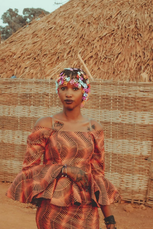 a woman standing in front of a hut with a flower in her hair, an album cover, trending on pexels, afrofuturism, somali attire, sitting down, body covered in floral tattoos, beautiful queen