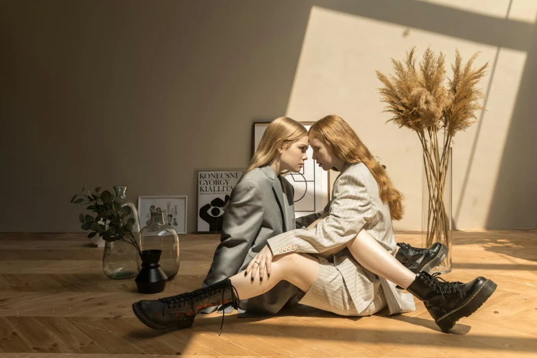 a couple of women sitting on top of a wooden floor, inspired by Elsa Bleda, trending on pexels, realism, kneehigh boots, lesbian kiss, mary jane ansell, sunlight