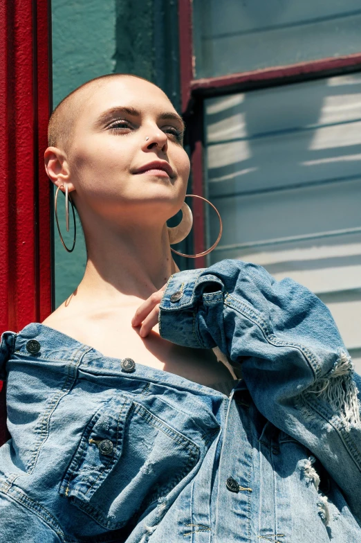 a woman standing in front of a red door, an album cover, trending on pexels, shaved bald head, denim jacket, on rooftop, an epic non - binary model