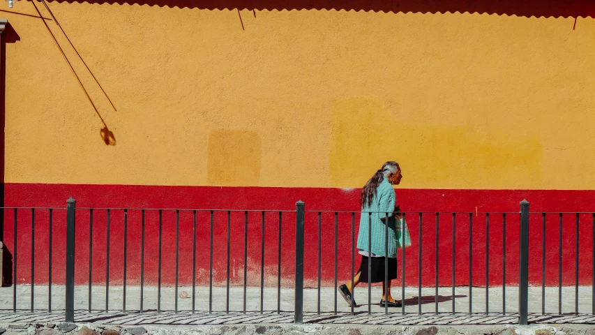 a woman walking down a street past a fence, pexels contest winner, color field, guanajuato, red and teal and yellow, african woman, medium format color photography