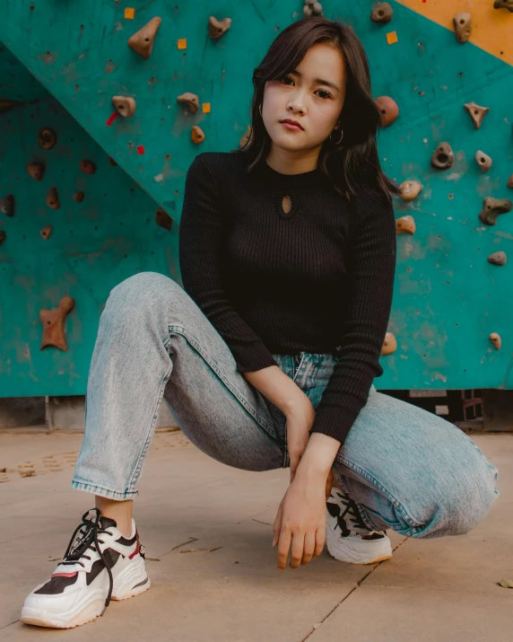 a woman sitting on the ground in front of a climbing wall, an album cover, trending on pexels, sneaker photo, asian women, portrait full body, ( ( ( wearing jeans ) ) )