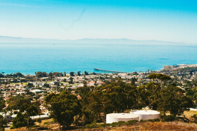 a view of the ocean from the top of a hill, by Ryan Pancoast, unsplash, the city of santa barbara, 1970s photo, on a bright day, town in the background