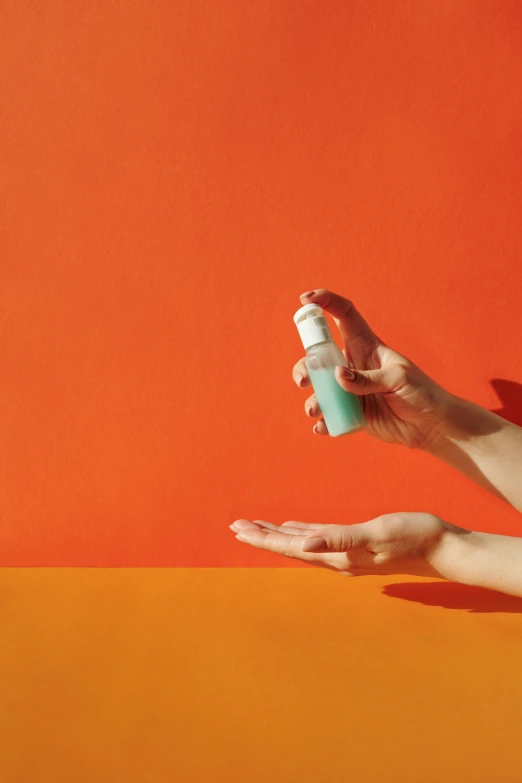 a woman laying on an orange surface holding a bottle of hand sanitizer, by Carey Morris, teal and orange color scheme, sleek hands, spraying liquid, skincare