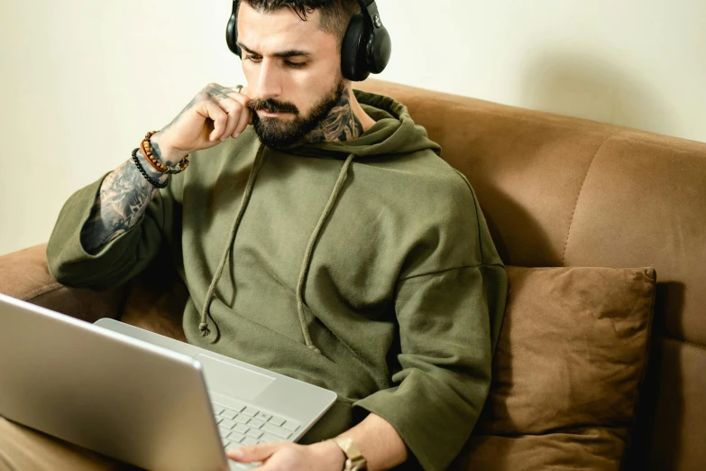 a man sitting on a couch with a laptop and headphones, inspired by Elsa Bleda, trending on pexels, tattooed man, beige hoodie, jacksepticeye, people at work