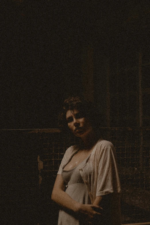 a woman in a white dress standing in a dark room, an album cover, inspired by Elsa Bleda, unsplash, tonalism, woman in a dark factory, grainy picture, looking threatening, ansel ]