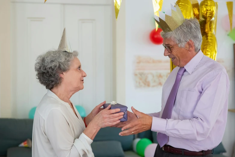a man giving a woman a birthday cake, by Alison Debenham, pexels contest winner, wearing a light grey crown, older male, holding gift, party hats