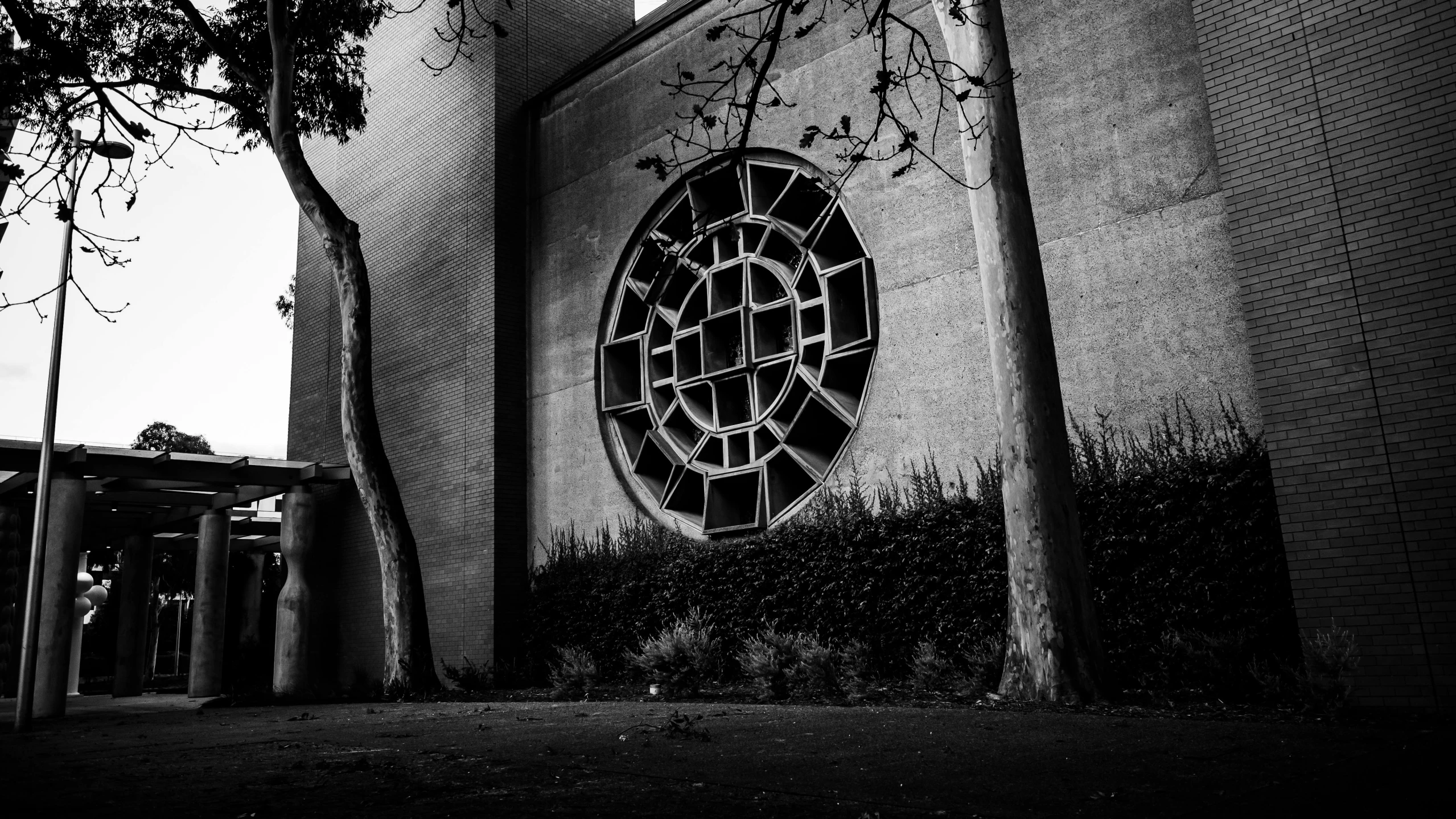 a black and white photo of a building with a circular window, inspired by Peter Basch, pexels contest winner, brutalism, trees around, stained glass futuristic church, death star, gardena architecture