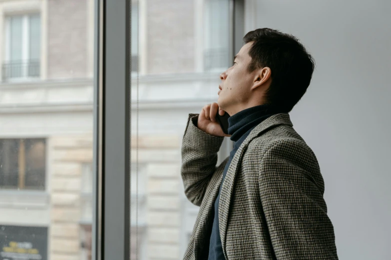 a man standing in front of a window looking out, trending on pexels, asian human, grey turtleneck coat, thinking pose, looking upwards