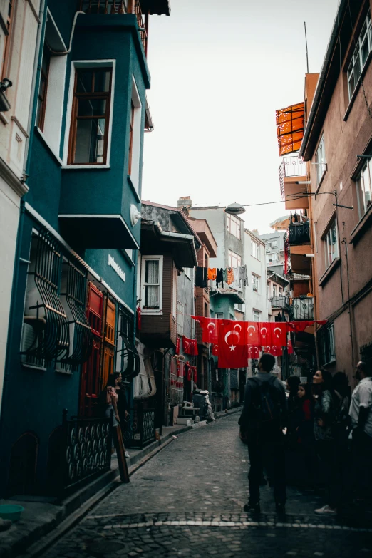 a group of people walking down a street next to tall buildings, a colorized photo, by Niyazi Selimoglu, pexels contest winner, hurufiyya, red banners, a quaint, alleys, cas