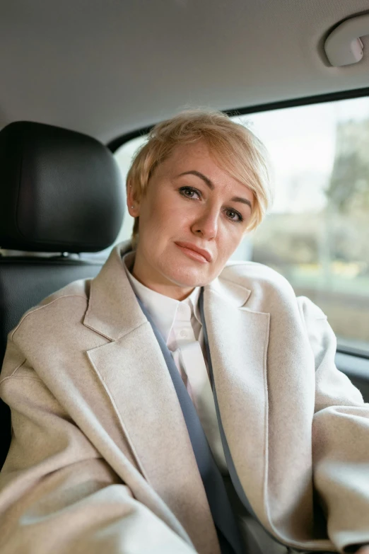 a woman sitting in the driver's seat of a car, inspired by Norma Bull, girl with short white hair, disappointed, wearing a fancy jacket, non binary model