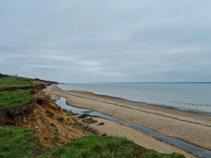 a body of water sitting on top of a sandy beach, a photo, by Thomas Barker, highfleet, looking down a cliff, grey sky, anya forger