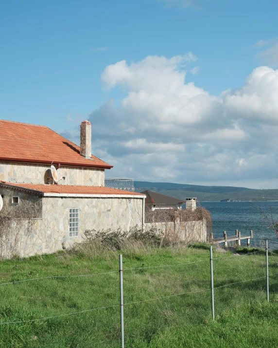 a house sitting on top of a lush green field, an album cover, by Tamas Galambos, pexels contest winner, renaissance, seaside, stone facade, brown, located in hajibektash complex