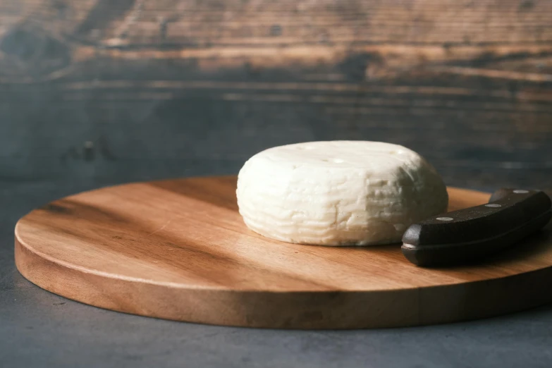 a piece of cheese sitting on top of a wooden cutting board, inspired by Théodule Ribot, unsplash, private press, smooth round rocks, vanilla, full product shot, byzantine