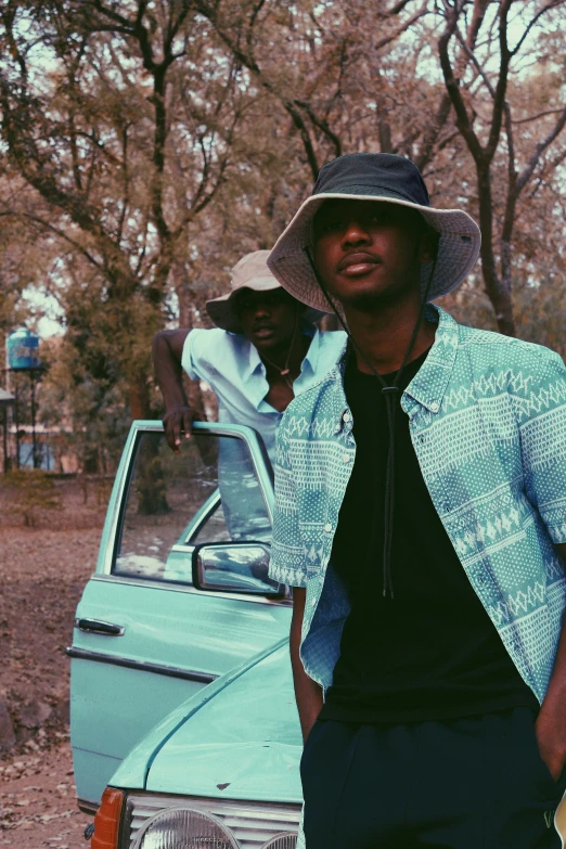 a man in a hat standing next to a car, an album cover, unsplash, two young men, ( ( dark skin ) ), teal aesthetic, in savannah
