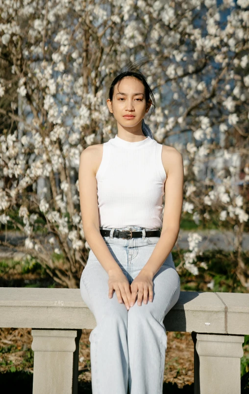 a woman sitting on a bench in front of a flowering tree, an album cover, inspired by helen huang, pexels, white tank top, kiko mizuhara, 15081959 21121991 01012000 4k, jeans and t shirt