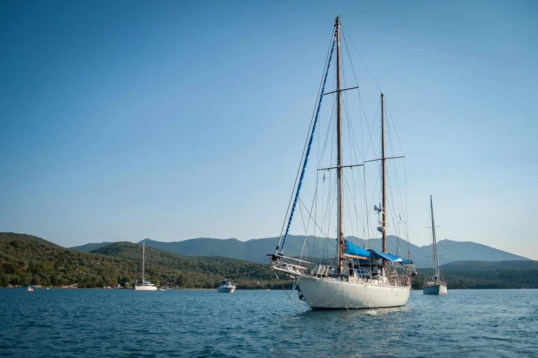 a sailboat in a body of water with mountains in the background, arabesque, picton blue, al fresco, exterior shot, clear blue skies