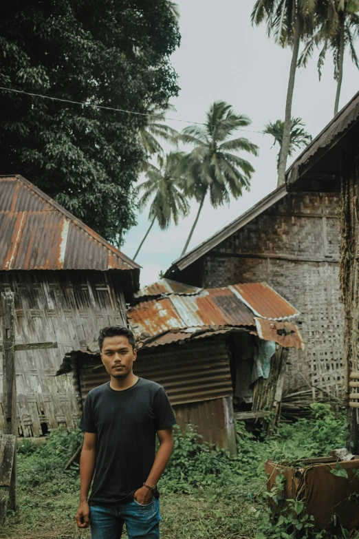 a man standing in front of a shack, an album cover, pexels contest winner, sumatraism, philippines, some houses in the background, background image, portrait of a slightly rusty