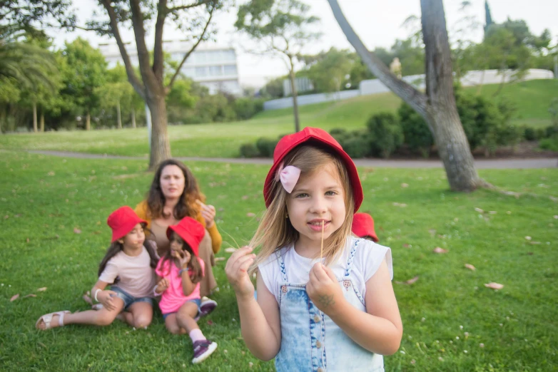 a little girl standing on top of a lush green field, an album cover, inspired by Elsa Beskow, pexels contest winner, realism, wearing a red backwards cap, on a hot australian day, time travelers appear in a park, holding maracas