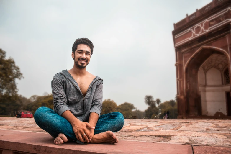 a man sitting on a ledge in front of a building, by Bernardino Mei, pexels contest winner, arabesque, a portrait of rahul kohli, standing over a tomb stone, while smiling for a photograph, markiplier