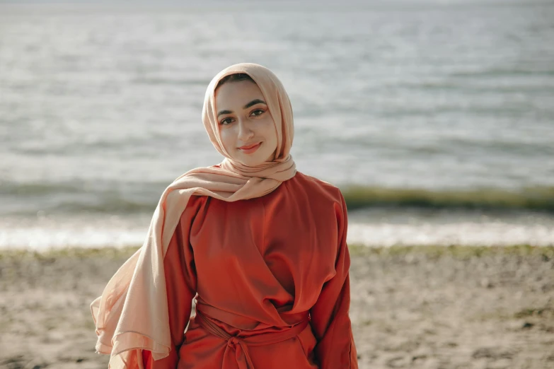 a woman standing on top of a sandy beach, inspired by Nazmi Ziya Güran, pexels contest winner, hurufiyya, red silk scarf, robe. perfect face, flowing salmon-colored silk, near a jetty