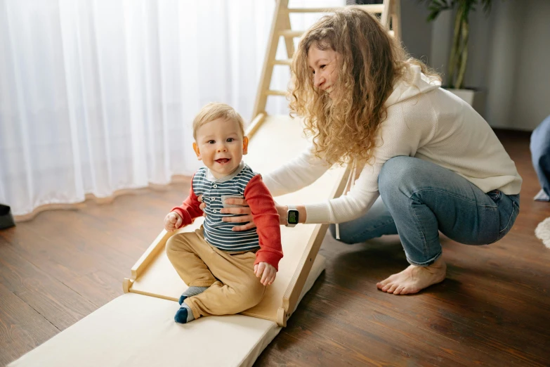 a woman playing with a toddler in a living room, a picture, wooden platforms, trying to ride it, profile image, small in size