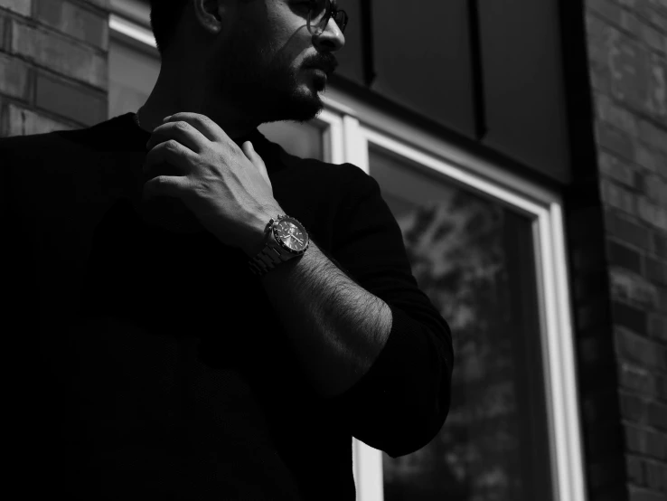 a man standing in front of a brick building, a black and white photo, by Emma Andijewska, pexels contest winner, wearing a watch, wearing black glasses, profile image, kyza saleem