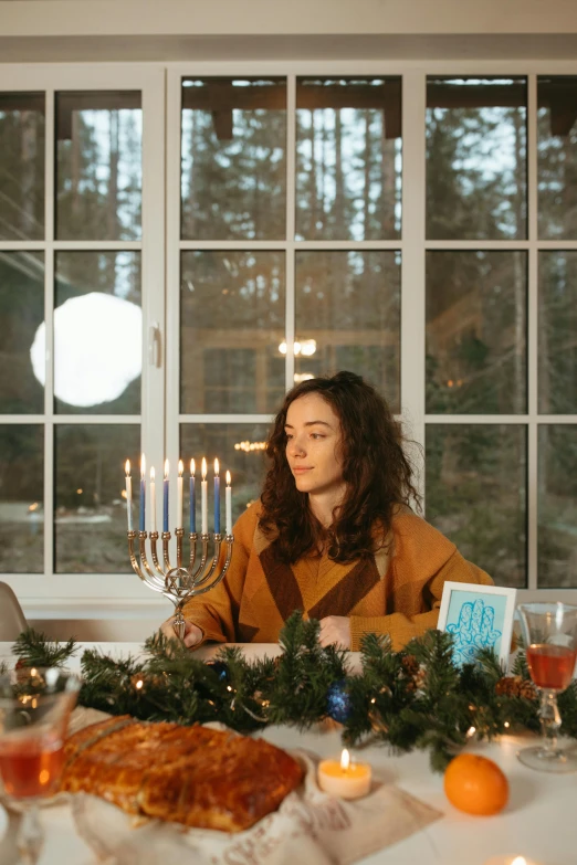 a woman sitting at a table with a cake and candles, sukkot, winter setting, profile image, still frame