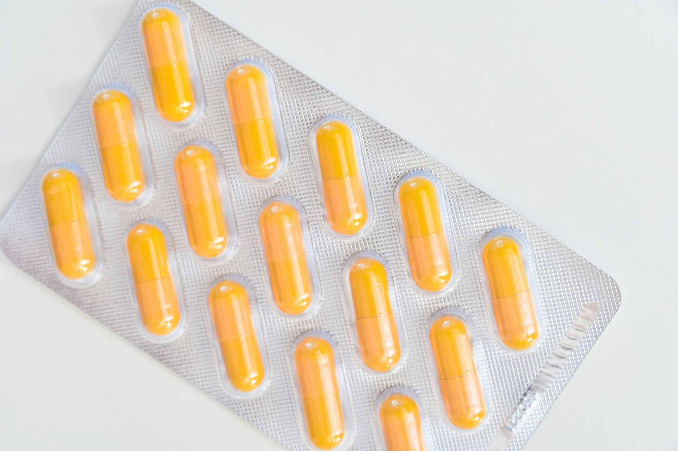 a pack of orange pills sitting on top of a white table, with a bright yellow aureola, lined up horizontally, 2000s photo, realistic »