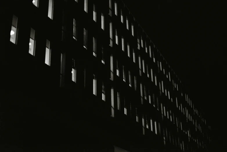 a black and white photo of a building at night, inspired by Paul Lucien Dessau, unsplash, brutalism, rows of windows lit internally, ilford hp 5, squares, dark hues