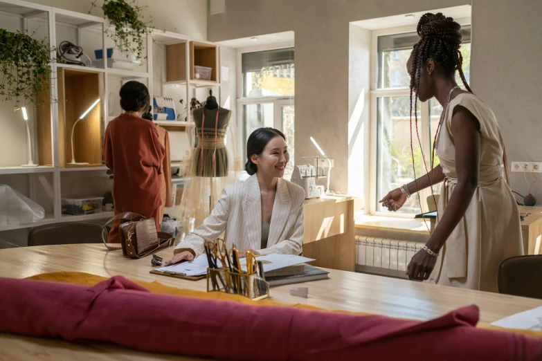 two women sitting at a table talking to each other, by Emma Andijewska, pexels contest winner, arbeitsrat für kunst, tailored clothing, lupita nyong'o, in a open-space working space, people shopping