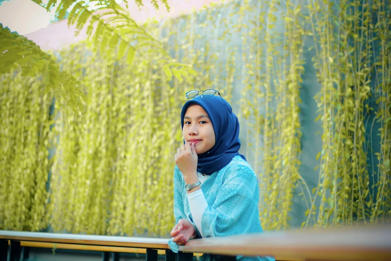 a woman sitting on a bench talking on a cell phone, a picture, inspired by Nazmi Ziya Güran, unsplash, hurufiyya, green and blue tones, background image, avatar image, malaysian