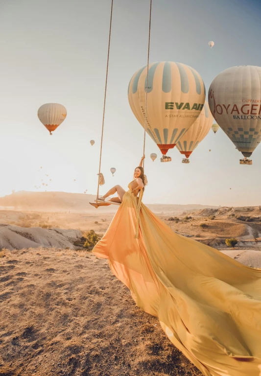 a woman in a yellow dress standing in front of hot air balloons, a picture, inspired by Oleg Oprisco, pexels contest winner, sand desert fantasy, 15081959 21121991 01012000 4k, waving, 8 k 4 k